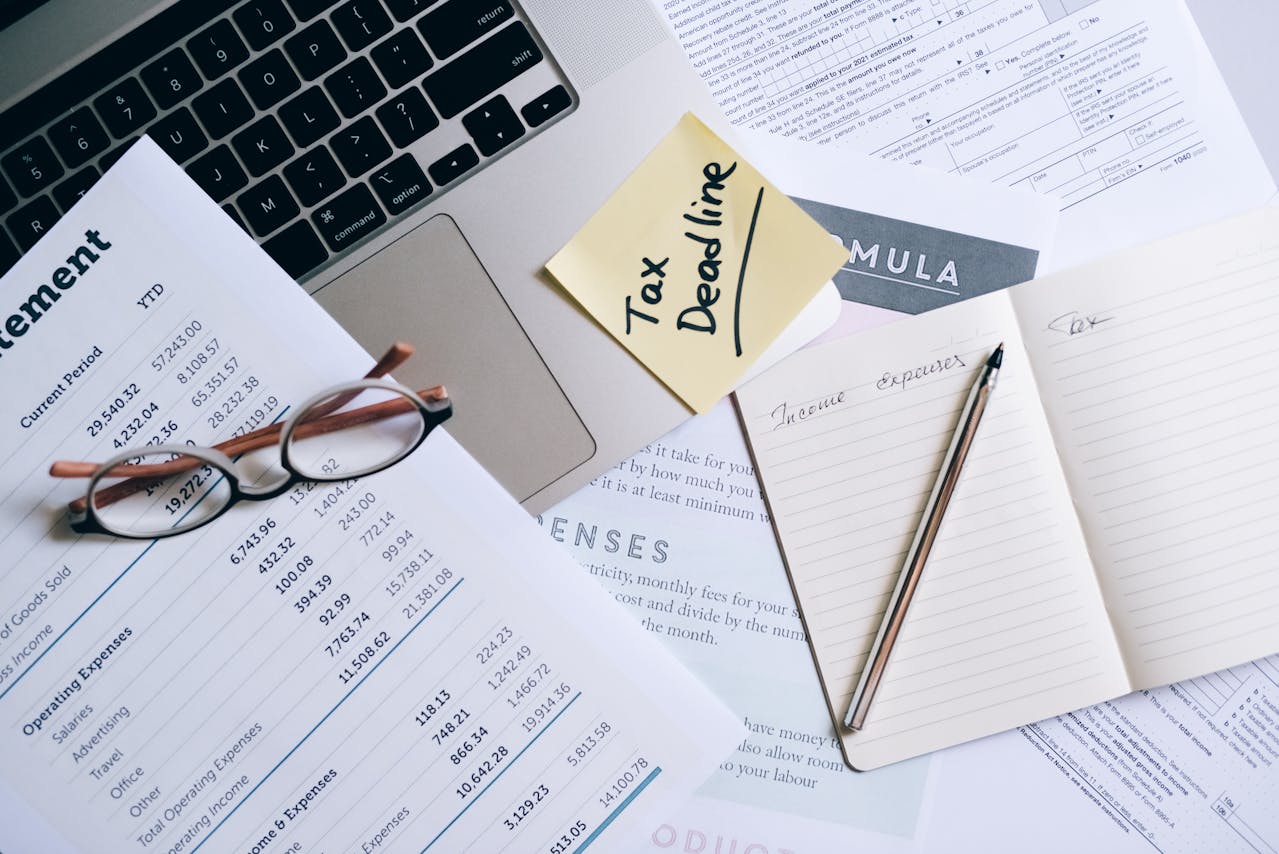 A Notebook and Pen Near the Laptop and Documents on the Table.